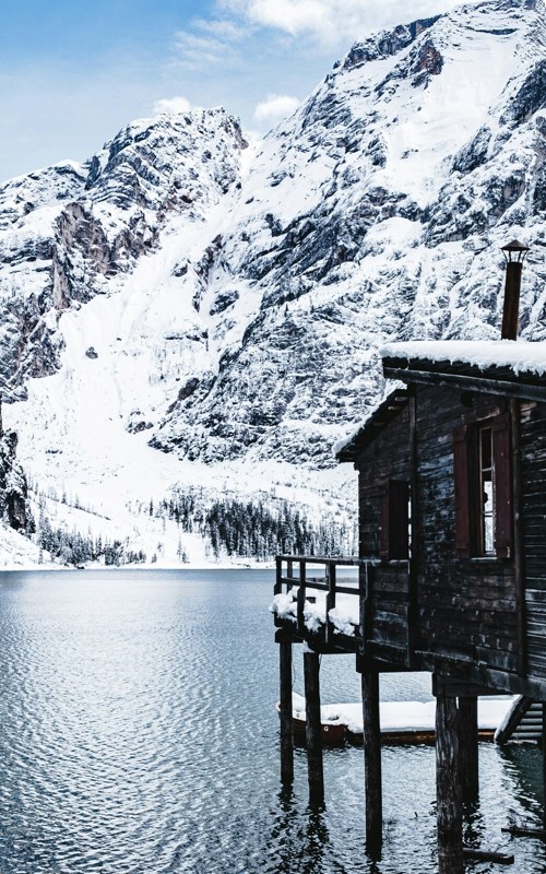 Exploring Lago di Braies in winter Wooden hut on stilts in the water of a lake, snow-covered mountain in the background
