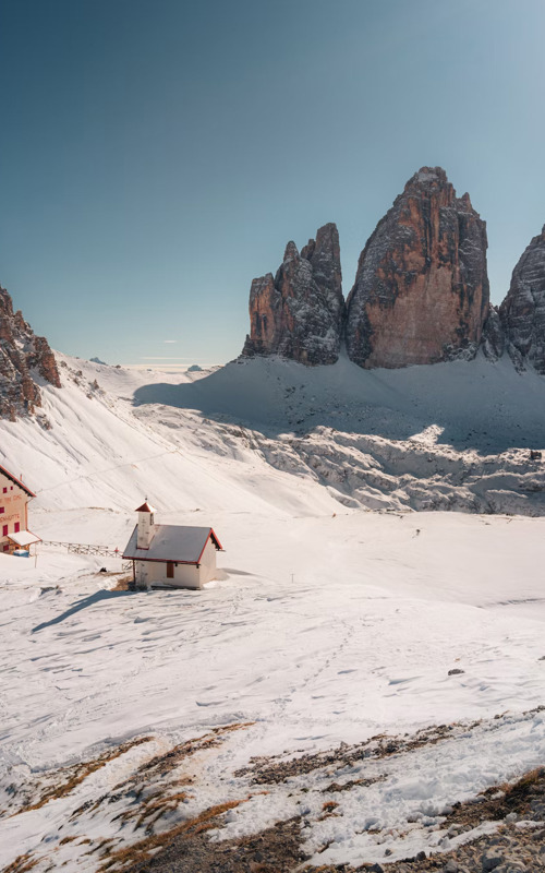 Tre Cime di Lavaredo in winter Hut and small church in a snowy landscape surrounded by Dolomites peaks